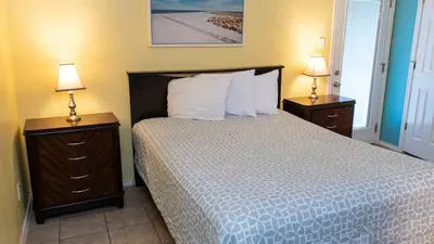 Rest easy in this inviting bedroom featuring a cozy serene bed, warm lighting, and coastal décor. With bedside tables, storage, and direct patio access, it’s a comfortable retreat perfect for recharging after a day at the beach.