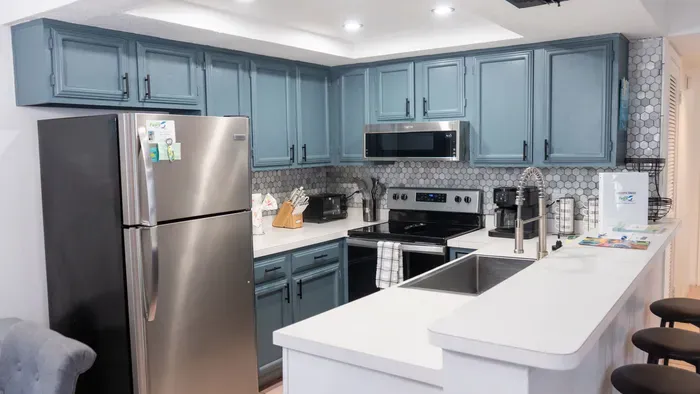 Modern kitchen with blue‑gray cabinetry, stainless appliances, and a bright island workspace. Patterned tile backsplash and thoughtful essentials create a clean, functional space perfect for cooking, gathering, and effortless vacation living.