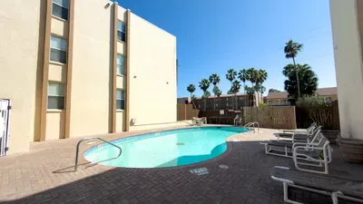 Private pool area with a curved design, lounge seating, and a quiet fenced setting. A sunny, relaxing spot perfect for unwinding, cooling off, and enjoying peaceful outdoor time just steps from your comfortable indoor retreat.