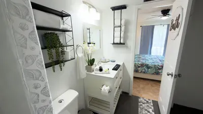 Elegant vanity setup with a bright countertop, framed mirror, and neatly arranged essentials. Fresh towels, greenery, and thoughtful touches create a clean, spa‑inspired bathroom space designed to elevate comfort and ease for every guest.