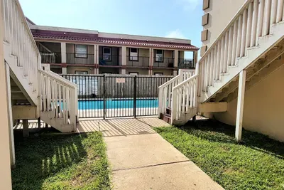 Inviting outdoor walkway leading to a secure, sparkling pool area, framed by bright white stairways, open balconies, and well‑kept grounds—an easy, sun‑filled community space that adds convenience, charm, and resort‑style appeal to every stay.