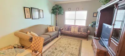 Airy, coastal‑inspired living and dining space featuring a glass‑top table, woven chairs, plush seating, and tropical greenery. Soft light and thoughtful décor create a warm, open layout perfect for relaxing, dining, and gathering together.