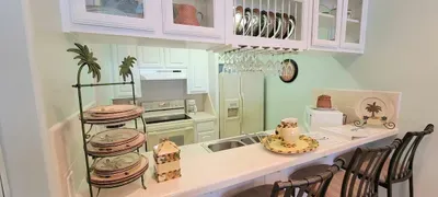Open, welcoming dining space with a glass‑top table, woven chairs, a spacious breakfast bar overlooking a bright, organized kitchen. Warm lighting, greenery, and thoughtful décor create an easy, comfortable setting for shared meals and gatherings.