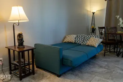 Cozy living area with a teal sofa bed, soft lighting, patterned pillows, and a nearby dining nook—creating a bright, functional space perfect for relaxing, reading, or accommodating extra guests with comfort and style.