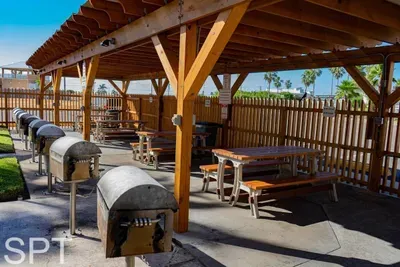 Spacious outdoor BBQ area featuring multiple grills, shaded picnic tables, and a clean, well‑kept setting surrounded by palms. A convenient communal space perfect for cookouts, gatherings, and enjoying warm coastal days with family and friends.
