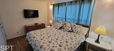 Relax in this bright coastal bedroom featuring a plush serene bed with seashell linens, soft lighting, a smart TV, and calming blue accents. A peaceful retreat designed for comfort, style, and effortless vacation living.
