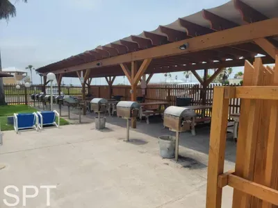 Outdoor BBQ pavilion featuring multiple grills, shaded picnic tables, and a clean, well‑kept setup surrounded by palms. A convenient communal space perfect for cookouts, gatherings, and enjoying warm coastal days with family and friends.