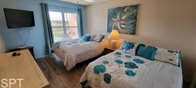 Bright and calming bedroom featuring two cozy beds with blue floral linens, warm lighting, and elegant artwork. Thoughtfully designed for comfort and relaxation, this inviting space offers a peaceful retreat perfect for unwinding after sun‑filled day