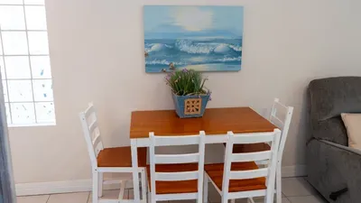 Enjoy meals or game night at a cozy dining table for four, adorned with cheerful beach art and a bright floral centerpiece. This inviting space is perfect for family breakfasts or unwinding after a sun-filled day at the beach