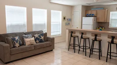 Relax in a sunny, open living space with a comfy sofa and beachy decor. The long breakfast bar with stylish stools is perfect for meals or game nights, making this spot ideal for family gatherings and laid-back vacation vibes.