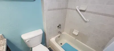 A bright, spotless bathroom featuring a granite vanity with warm accents, a neatly tiled tub, soft blue walls, and thoughtful touches like fresh flowers and essentials, creating a clean, comfortable space designed for a relaxing, guest‑friendly stay.