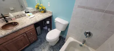 A clean, well‑kept bathroom featuring a granite vanity with warm accents, a neatly tiled tub, soft blue walls and thoughtful touches like fresh flowers and essentials, creating a bright, comfortable space designed for a relaxing, guest‑friendly stay.