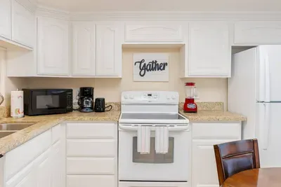 Cozy "Gather" Kitchen Haven
Bright white cabinetry, granite counters, stainless appliances, and ample storage define this inviting kitchen. Fridge, stovetop, microwave, and coffee maker ready for meals; "Gather" sign sets warm hosting vibe.