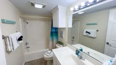 Bright Beachy Bathroom Escape
Spacious tub-shower combo with turquoise curtain, fresh towels & potted plant welcomes you. Vanity mirror, bright lights "Salty Hair" sign & ample storage keep it clean & coastal—perfect for refreshing after beach vibes.