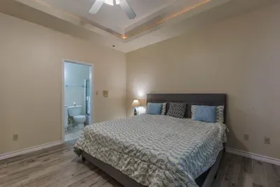Alt shot of master bedroom. California King Tempurpedic bed with full en suite bathroom / tub/shower off it. Wood look hard tile, trellis ceiling super duper high. Has a 50" flat screen in it with cable too