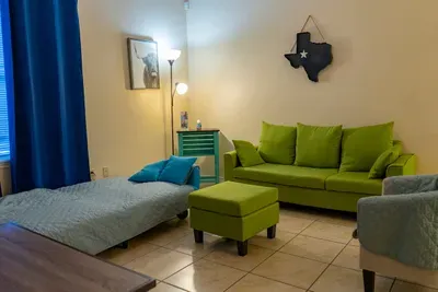 Bright, inviting living space featuring a comfy green sofa, cozy daybed, warm lighting, and playful Texas‑themed décor. A versatile, guest‑friendly room offering comfort, color, and a relaxed setup perfect for unwinding or gathering during any stay.