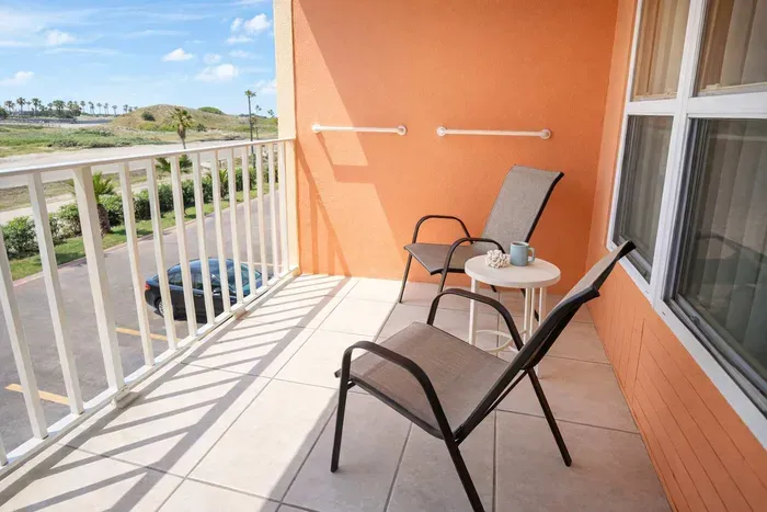Sunlit balcony with palm view, mesh chairs, and accessibility features—perfect for morning coffee or evening breeze. Close to beach, parking, and tropical greenery.