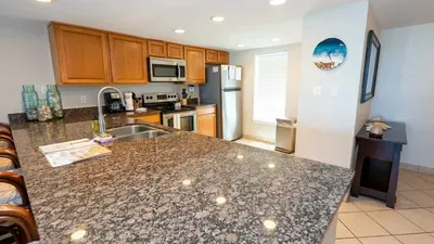 Warm, modern kitchen featuring granite countertops, stainless‑steel appliances and inviting bar seating perfect for casual dining or gathering. Thoughtful lighting and clean design create a welcoming space for cooking, hosting and relaxing together.