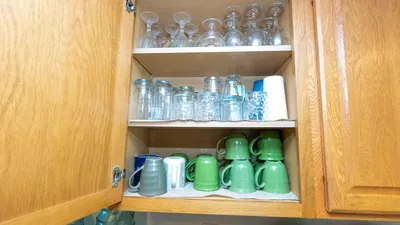 Thoughtfully organized drinkware cabinet featuring wine glasses, tumblers, and colorful mugs arranged for easy access. A clean, well‑stocked setup that ensures guests have everything they need for coffee, cocktails and everyday convenience.