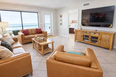 Sunlit coastal living room featuring caramel leather seating, a sleek entertainment console, and ocean views through glass doors. Bright, airy, and styled for comfort—perfect for relaxing after beach days or cozy evenings in your South Padre getaway.