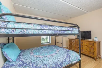 This bright bunk room features sturdy metal frames, coordinated blue bedding, soft accent rugs, and a dresser with TV—offering a practical, comfortable setup ideal for siblings, friends, or extra guests during your coastal stay.