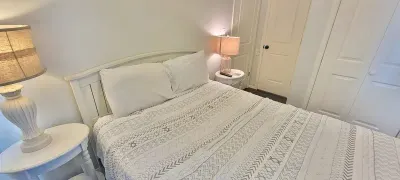 Bright, calming bedroom featuring a plush serene bed with crisp white linens, warm ambient lighting, dual bedside lamps, and clean modern finishes—designed to offer guests a peaceful, comfortable retreat with effortless relaxation.