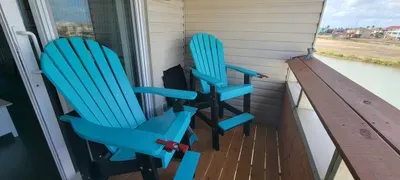 Charming waterfront balcony featuring vibrant Adirondack chairs, warm wood decking, and peaceful open‑air views—offering guests a relaxing outdoor retreat perfect for morning coffee, sunset lounging, and unwinding in a calm coastal setting.