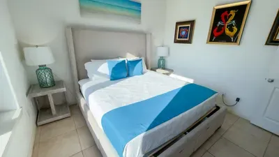 Artistic Coastal Bedroom Retreat
Comfortable bed with turquoise accents and plush bedding anchors this serene guest room, bathed in soft light. Vibrant art and seaglass lamps evoke beachy elegance—perfect for restful nights after seaside days!