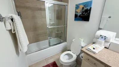 Sunny Tub-Shower Bathroom
Spotless bathroom features glass shower-tub combo, granite vanity, and plush rolled towels. Sunset beach art adds tropical flair—quick rinse after pool or beach, all in clean, inviting comfort!