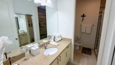 Spa-Like Bathroom Haven
Granite vanity with dual sinks, fluffy towels, and bright lighting sets a serene tone in this pristine bath. Shiplap accents and cross decor add coastal charm—indulge in refreshing showers daily!