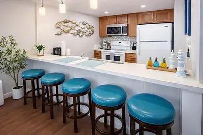 Bright, welcoming kitchen with warm wood tones and coastal pops of turquoise. A clean, airy space that feels instantly relaxing — perfect for slow mornings, shared meals, and effortless vacation living.