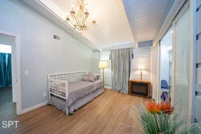Airy, cottage‑coastal bedroom featuring a bright daybed, vaulted ceilings, soft blue walls, warm wood floors, and a cozy reading nook. Natural light, relaxed textures, and thoughtful décor create a peaceful retreat perfect for unwinding.