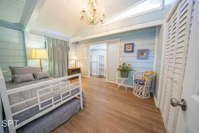 Charming coastal-inspired bedroom featuring a bright daybed setup, vaulted ceilings, soft blue walls, warm wood flooring, and cozy seating. Thoughtful décor, natural light, and relaxing textures create a peaceful retreat perfect for unwinding.