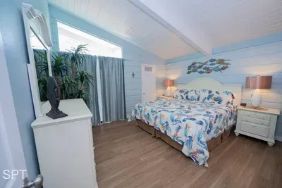 Calming beach‑themed bedroom featuring a cozy  bed, blue paneled walls, warm wood floors, and soft ambient lighting. Thoughtful décor and airy design elements create a soothing space perfect for relaxing after a full day by the coast.