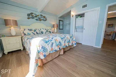 Bright coastal bedroom featuring a plush serene bed, soft blue paneling, warm wood floors, and amazing décor. Thoughtful lighting, airy design, and relaxing beach‑inspired accents create a calm retreat perfect for unwinding after sun‑filled days.