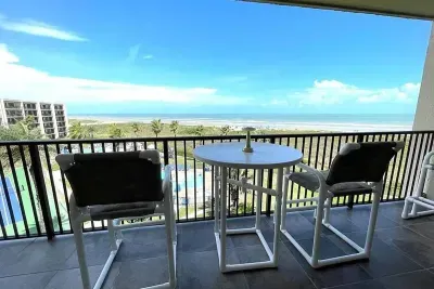 Private balcony overlooking sparkling pools, palm‑lined grounds and the ocean beyond. The inviting table setup and open‑air views create a guest‑ready retreat perfect for coffee, cocktails, and peaceful vacation downtime.