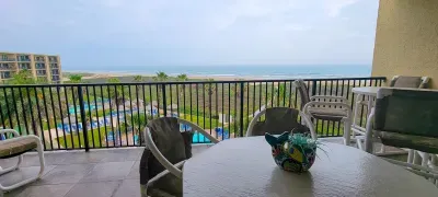 Balcony with sweeping views of pools, palm trees and the shoreline, paired with a cozy table setup perfect for relaxing. The bright coastal scenery creates a guest‑ready space ideal for morning coffee, sunset moments and unwinding outdoors.