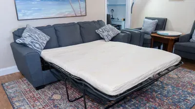 This inviting living space features a comfortable sofa bed, soft lighting, and a colorful rug that adds warmth and charm. Ideal for extra guests, it offers a practical, cozy setup perfect for relaxing, lounging, and flexible sleeping arrangements.