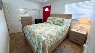 This bright, cozy bedroom features a comfortable bed with soft linens, warm natural light, and simple, functional furnishings. A peaceful retreat designed for restful nights and relaxed mornings, offering a clean, inviting space to unwind.