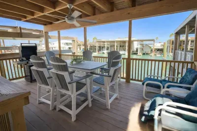 Waterfront deck with dining, lounge seating, ceiling fan, and canal views—perfect for grilling, relaxing, and entertaining in coastal comfort. Steps from boat slips and stilted beach homes.