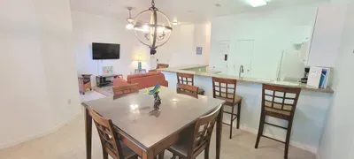 Bright open‑concept living, dining, and kitchen space featuring a modern chandelier, cozy seating, and a sleek breakfast bar. Perfect for gathering, relaxing, and enjoying effortless flow throughout this inviting coastal‑inspired layout.