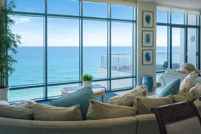 Oceanfront Living Room with Panoramic Views — Spacious, sunlit interior featuring floor-to-ceiling windows, coastal décor, and direct balcony access overlooking the sea. Ideal for relaxing getaways and scenic stays.