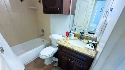 Clean, well‑organized bathroom featuring a granite vanity, warm wood cabinetry, and a neatly tiled tub‑shower combo. Thoughtful essentials, soft lighting, and a tidy layout create a comfortable, practical space for guests during their stay.