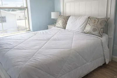 Bright, serene bedroom with crisp white bedding, geometric accent pillows, and natural light—perfect for restful stays and stylish comfort.