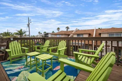 Tropical deck retreat with 6 vibrant Adirondack chairs, lush palm views, and colorful rug—perfect for morning coffee or sunset chats in a coastal neighborhood. Relax, unwind, and soak in the beachside vibes.