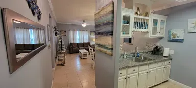 An inviting open‑concept space with a bright kitchen, granite counters & glass‑front cabinetry flows into a cozy living area with a sectional sofa & natural light. Clean décor, warm tones, and thoughtful details create a comfortable, guest‑ready set.