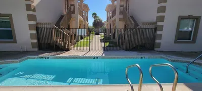 A bright, inviting pool area set between well‑kept buildings offers guests a refreshing place to unwind. Clear blue water, palm‑lined pathways, and sunny open spaces create a relaxed, resort‑style atmosphere perfect for enjoying warm coastal days.