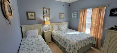 A bright, coastal‑themed bedroom with twin and comfortable beds, soft seashell décor, and calming blue walls offers a relaxing retreat. Thoughtful touches, natural light, and a clean, welcoming layout create a comfortable space perfect for families.