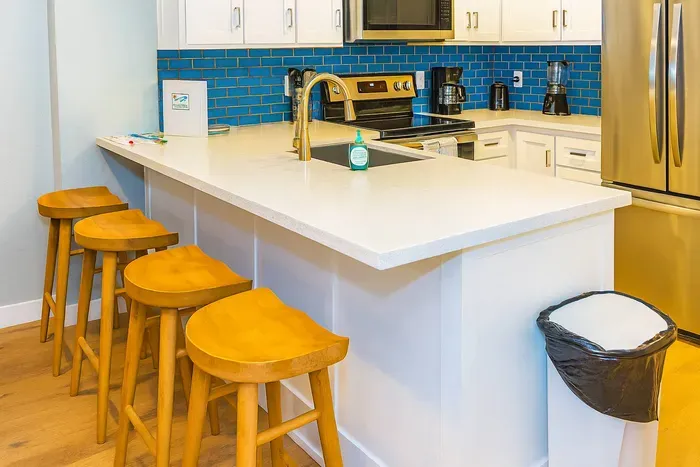 Cook and connect in this modern kitchen featuring sleek quartz countertops, stainless steel appliances and stylish blue tile backsplash. Perfect for casual breakfasts or entertaining guests, the nearby bar seating adds a warm, inviting touch.