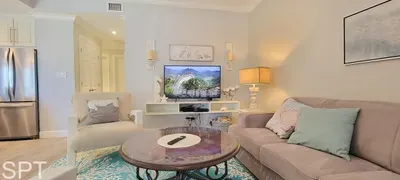 Coastal‑inspired living room with soft tones, modern seating, and an open kitchen — a bright, inviting space designed for comfort and relaxation.